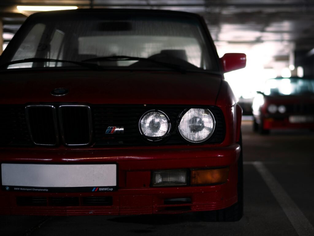 Front view of a vintage red BMW M series car in a dimly lit parking garage.